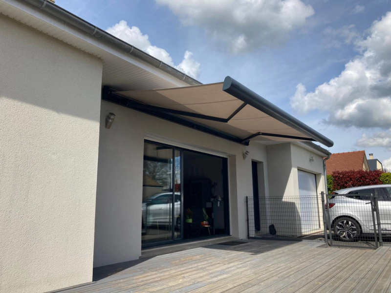 Store banne beige déployé, bras anthracite, au-dessus baie noire et terrasse bois