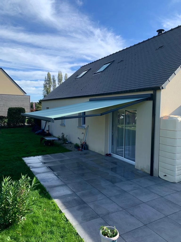 Store banne vert menthe, armature anthracite, terrasse carrelée, toiture ardoise