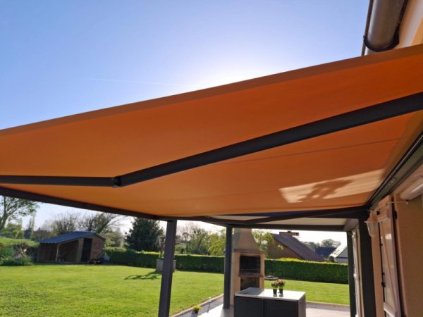 Store banne orange déployé, bras anthracite, terrasse pierre et barbecue maçonné