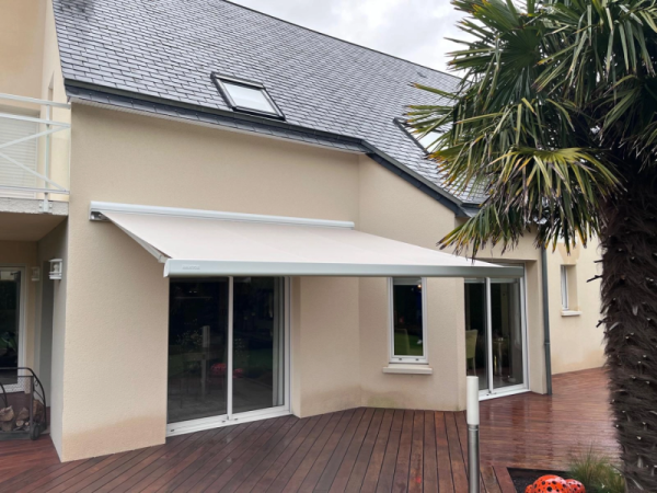 Store banne crème déployé au-dessus d'une terrasse bois devant baie vitrée blanche