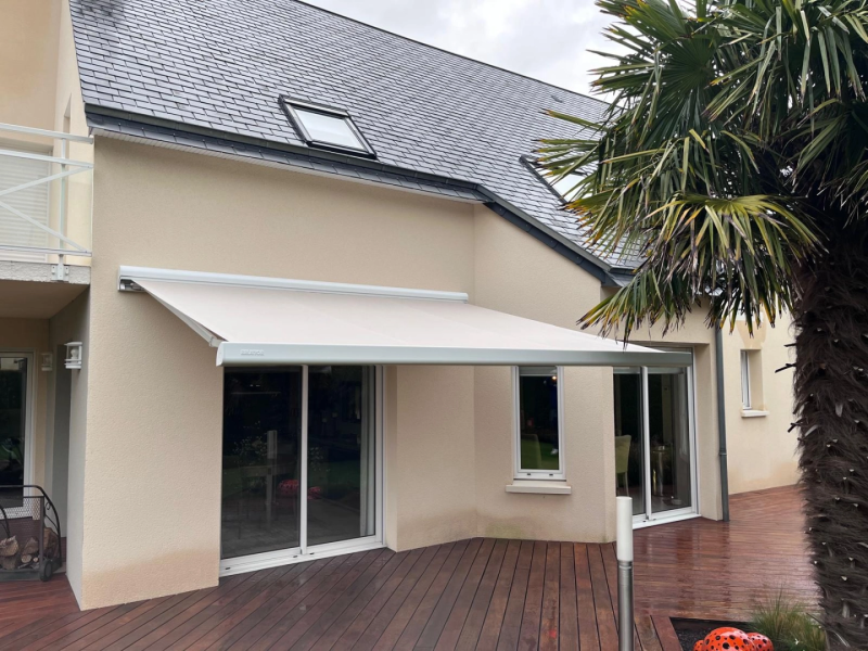 Store banne crème déployé au-dessus d'une terrasse bois devant baie vitrée blanche