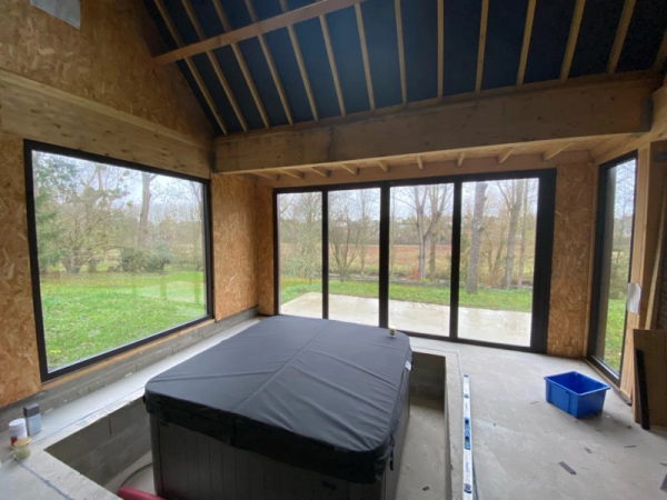 Spa encastré dalle béton, baies pliantes alu noir, ossature bois OSB, chantier