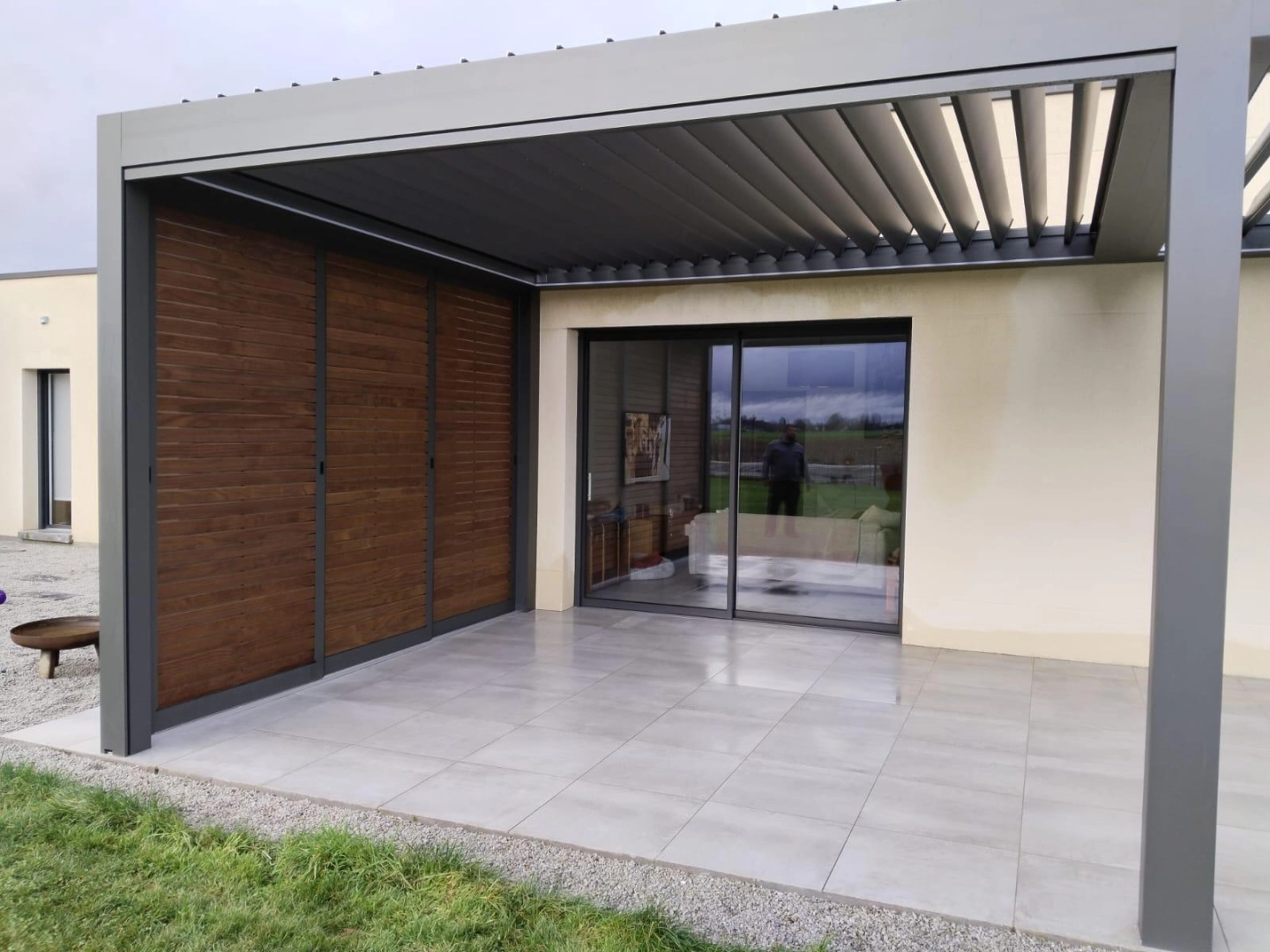 Pergola bioclimatique grise, lames orientables, claustras bois coulissants, terrasse