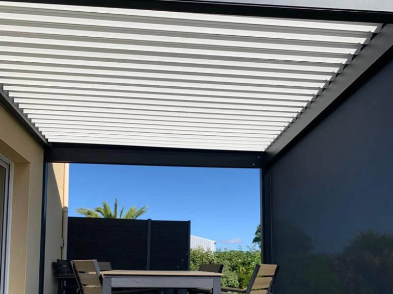 Pergola bioclimatique anthracite, lames blanches, screen latéral gris, table jardin