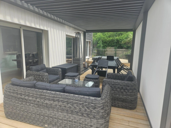 Pergola bioclimatique anthracite, store latéral gris, terrasse bois et salon rotin