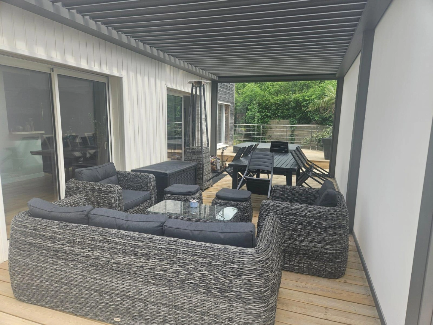 Pergola bioclimatique anthracite, store latéral gris, terrasse bois et salon rotin