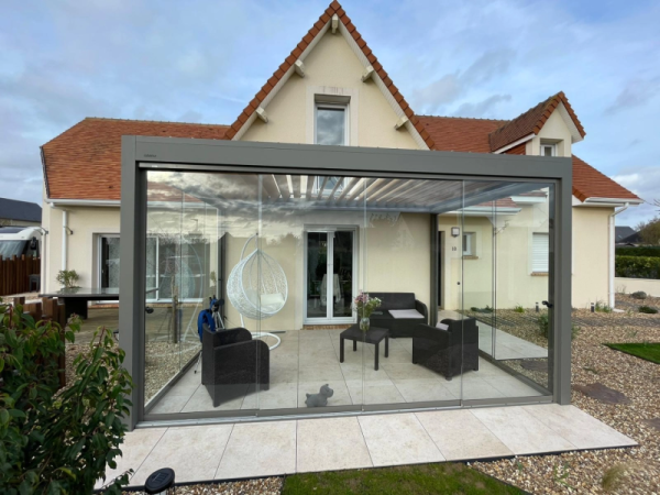 Pergola bioclimatique anthracite, lames blanches, parois vitrées, terrasse beige