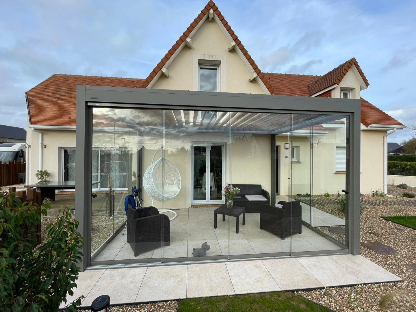 Pergola bioclimatique anthracite, lames blanches, parois vitrées, terrasse beige