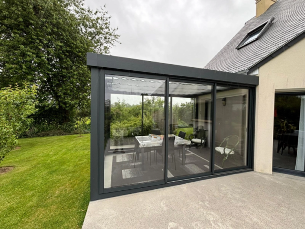 Véranda alu anthracite toit verre, store plissé blanc, salle à manger et jardin vert