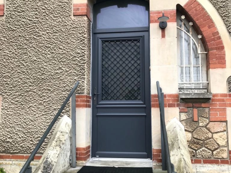Porte d'entrée gris anthracite, vitrage et grille fer, imposte cintrée, mur pierre