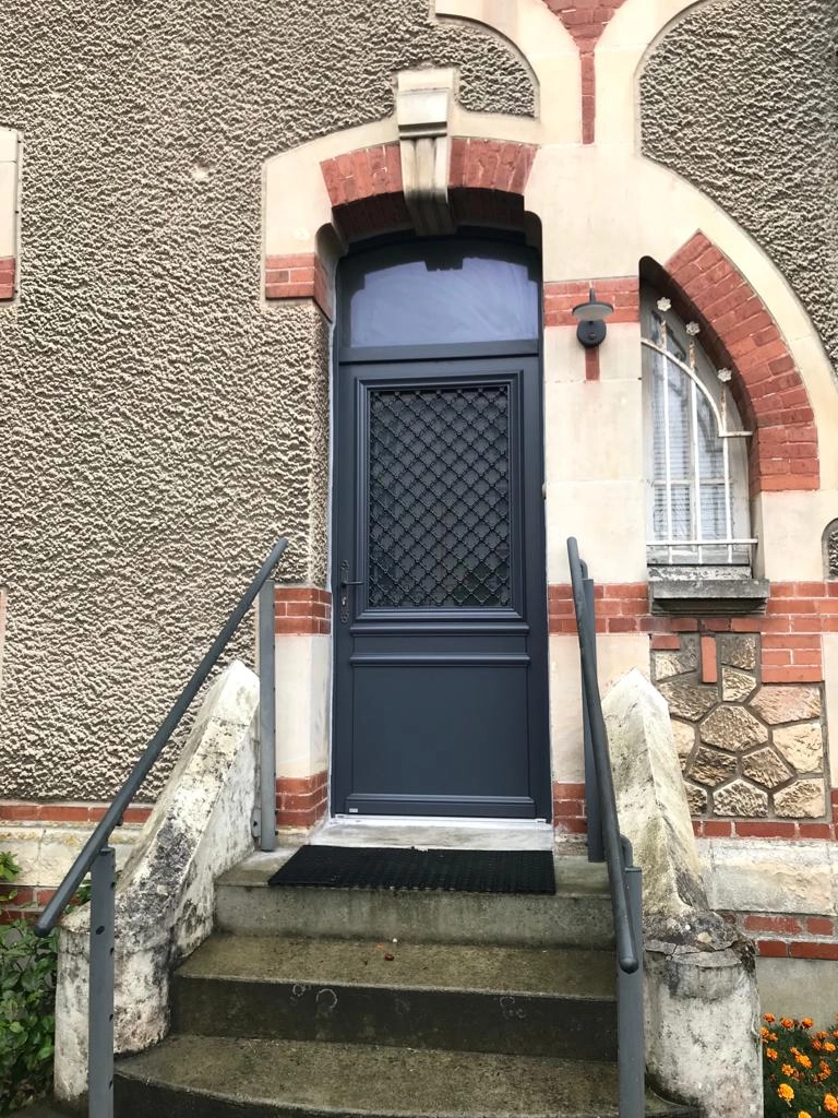 Porte d'entrée gris anthracite, vitrage et grille fer, imposte cintrée, mur pierre