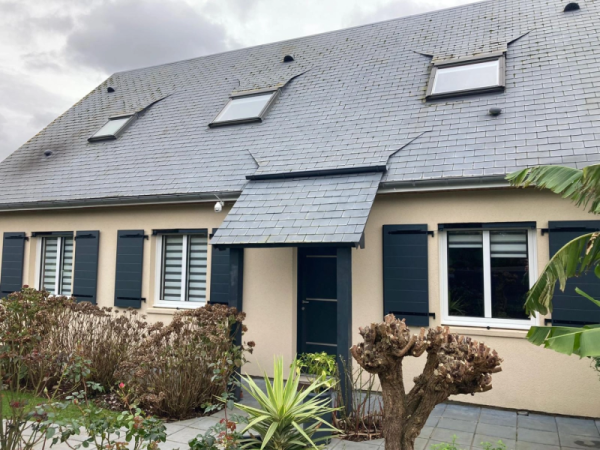 Façade crème, volets battants anthracite, porte sous auvent ardoise, velux toit