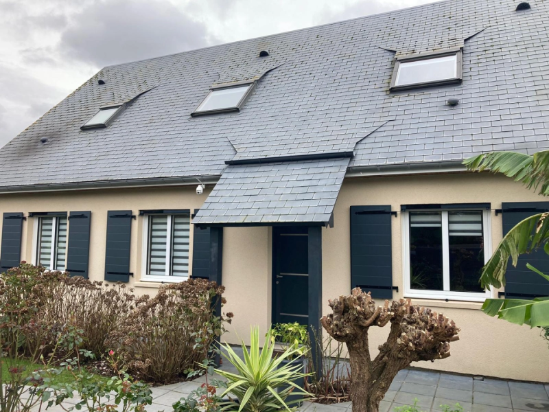 Façade crème, volets battants anthracite, porte sous auvent ardoise, velux toit