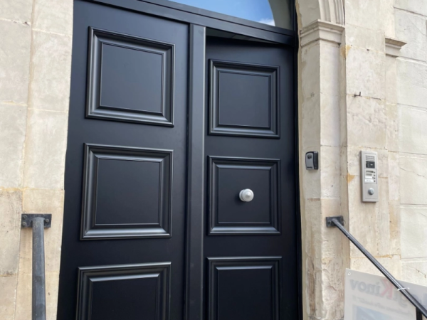 Porte d'entrée double vantaux noirs à panneaux moulurés, encadrement pierre claire