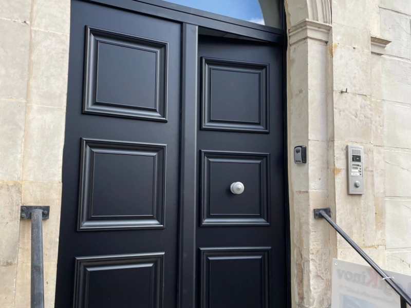 Porte d'entrée double vantaux noirs à panneaux moulurés, encadrement pierre claire