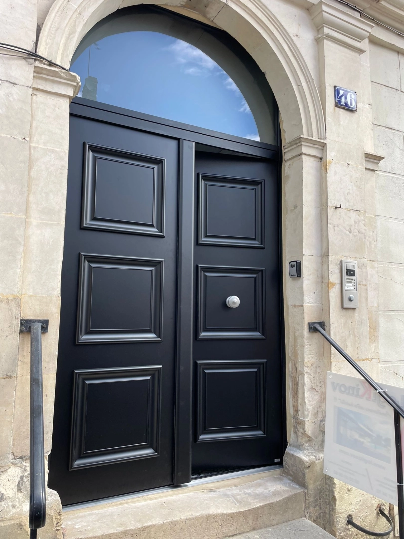 Porte d'entrée double vantaux noirs à panneaux moulurés, encadrement pierre claire