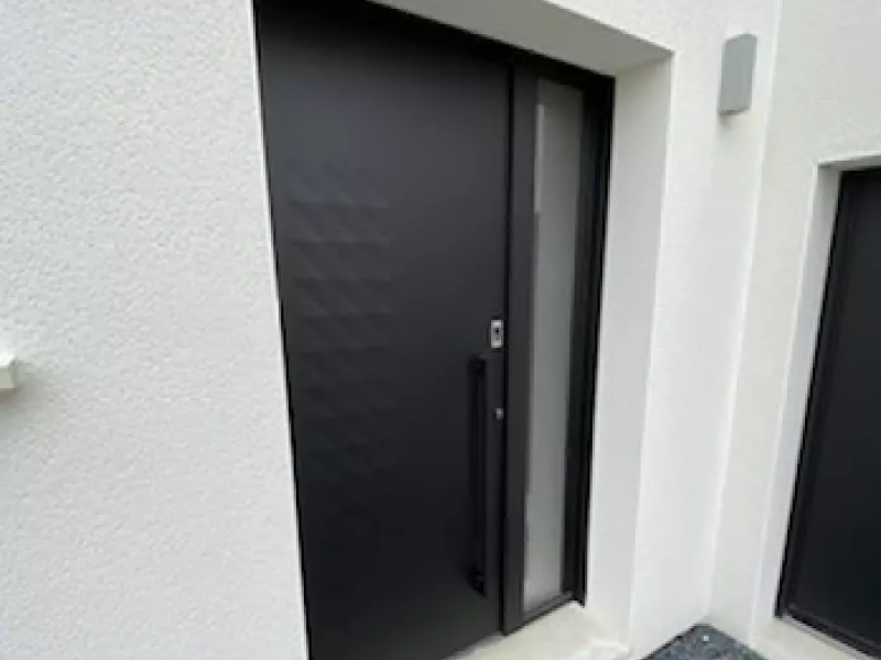 Porte d'entrée alu noir mat, imposte dépolie, poignée verticale, encadrement enduit blanc