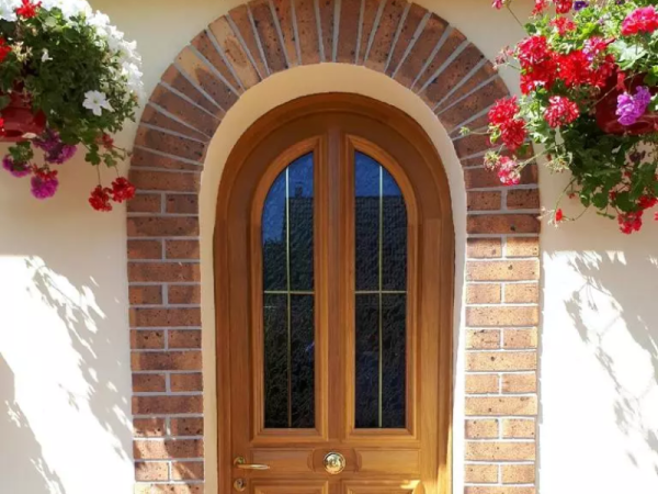Porte d'entrée cintrée en bois clair, vitrage petits bois laiton, arche en briques rouges