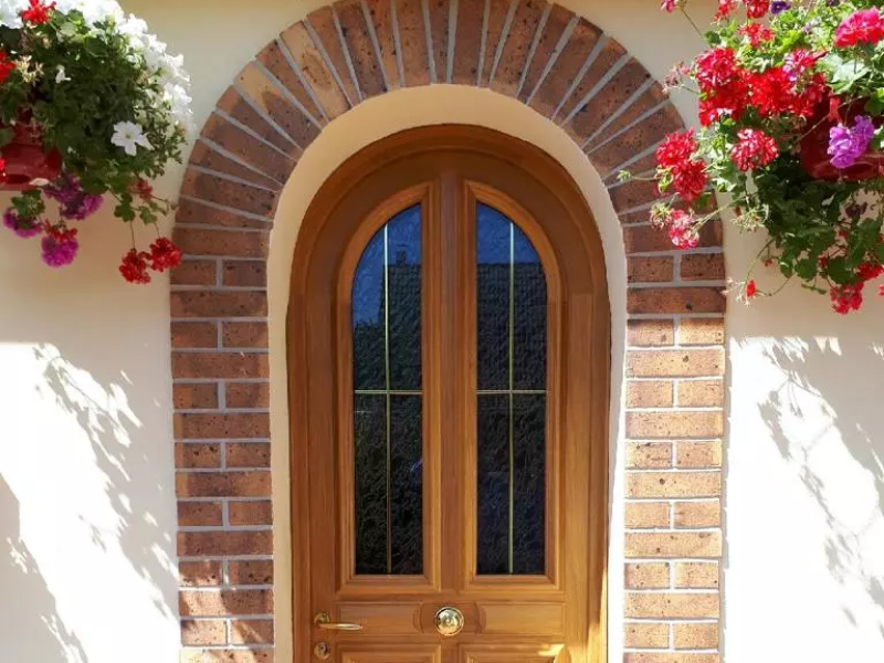 Porte d'entrée cintrée en bois clair, vitrage petits bois laiton, arche en briques rouges