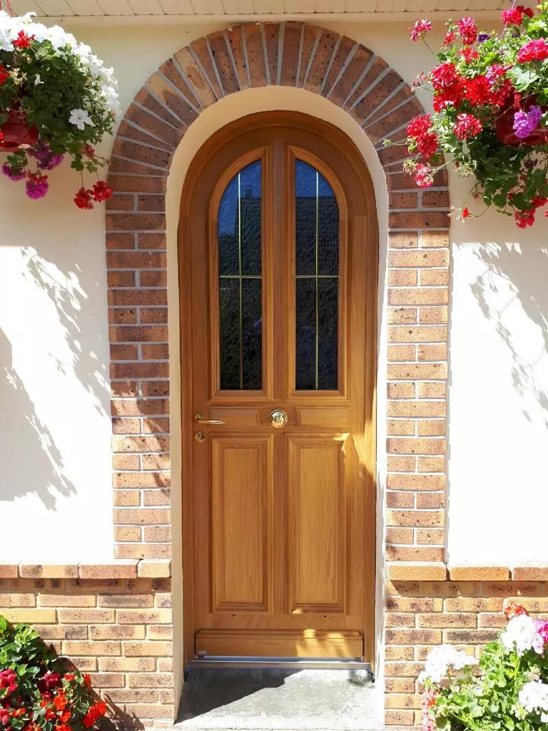 Porte d'entrée cintrée en bois clair, vitrage petits bois laiton, arche en briques rouges