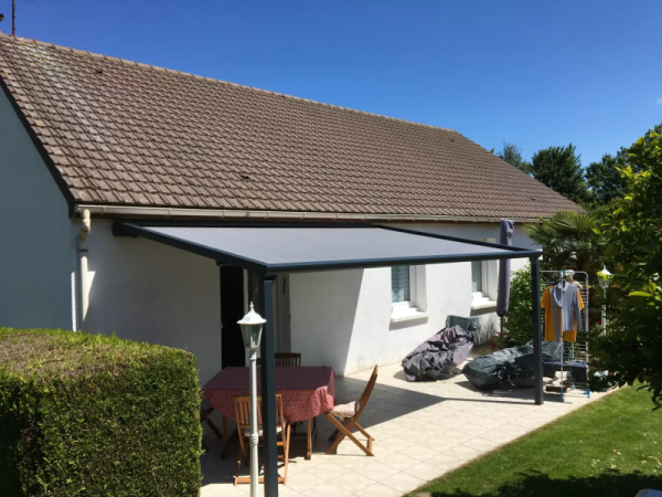 Pergola adossée alu anthracite, toile grise rétractable, terrasse carrelée et salon de jardin
