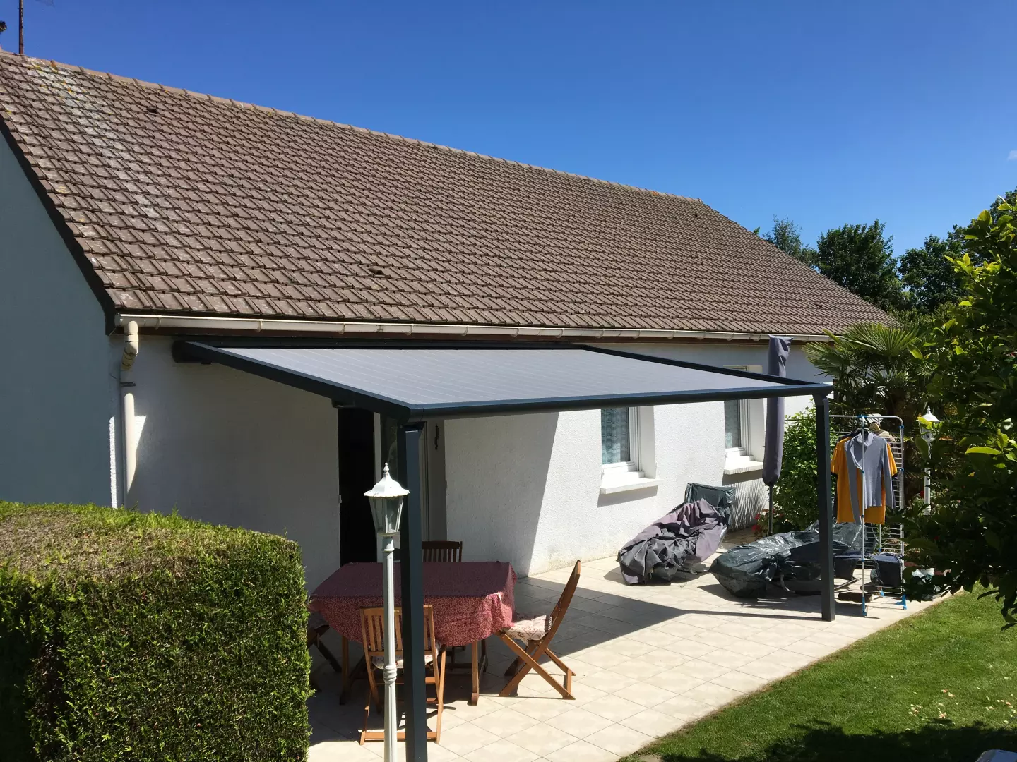 Pergola adossée alu anthracite, toile grise rétractable, terrasse carrelée et salon de jardin