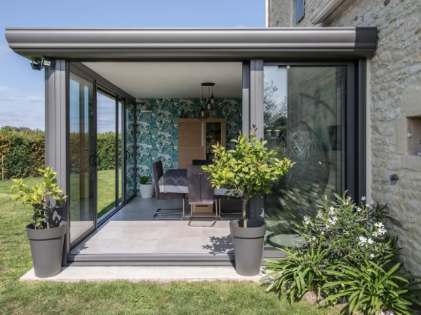 Véranda toit plat alu gris architecte, baies coulissantes, maison pierre et pelouse