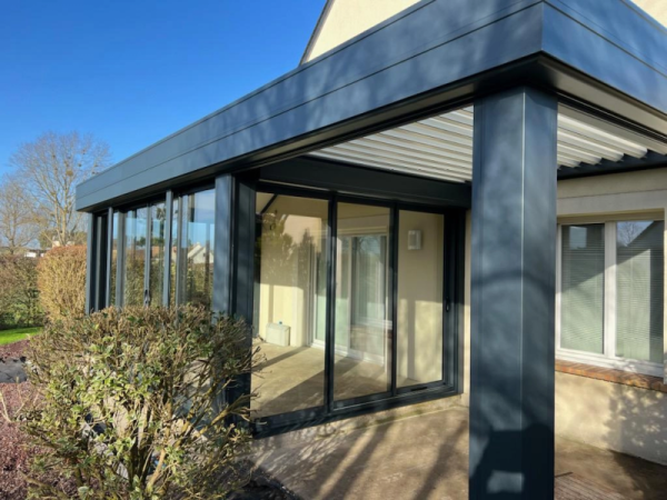 Pergola bioclimatique anthracite adossée, lames claires, paroi vitrée, dalle béton