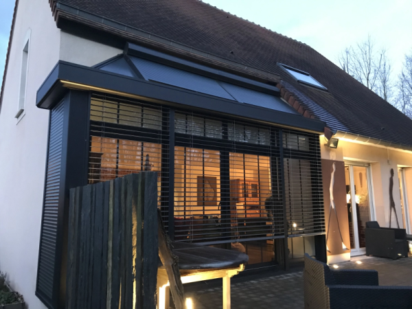 Extension alu noir, brise-soleil intégrés, éclairage LED, terrasse pavée au crépuscule