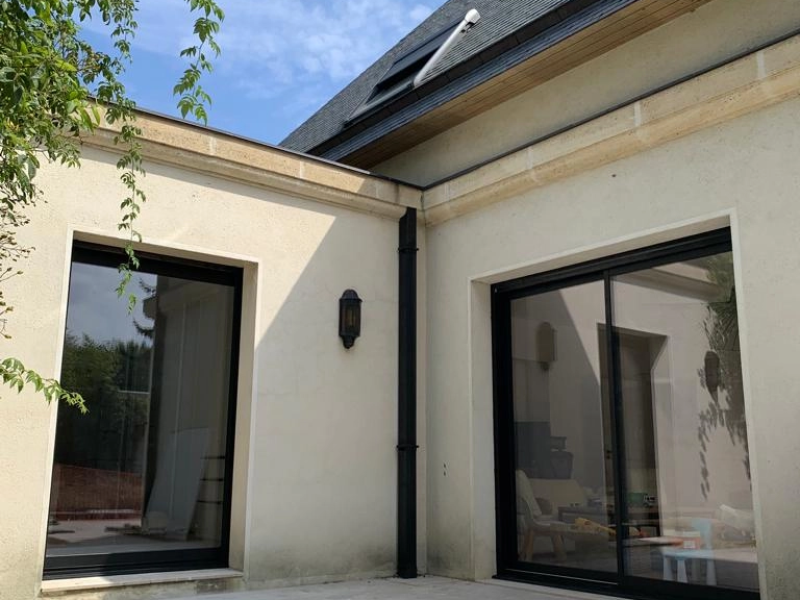 Baie coulissante alu noir et fenêtre fixe, façade beige pierre, toiture ardoise