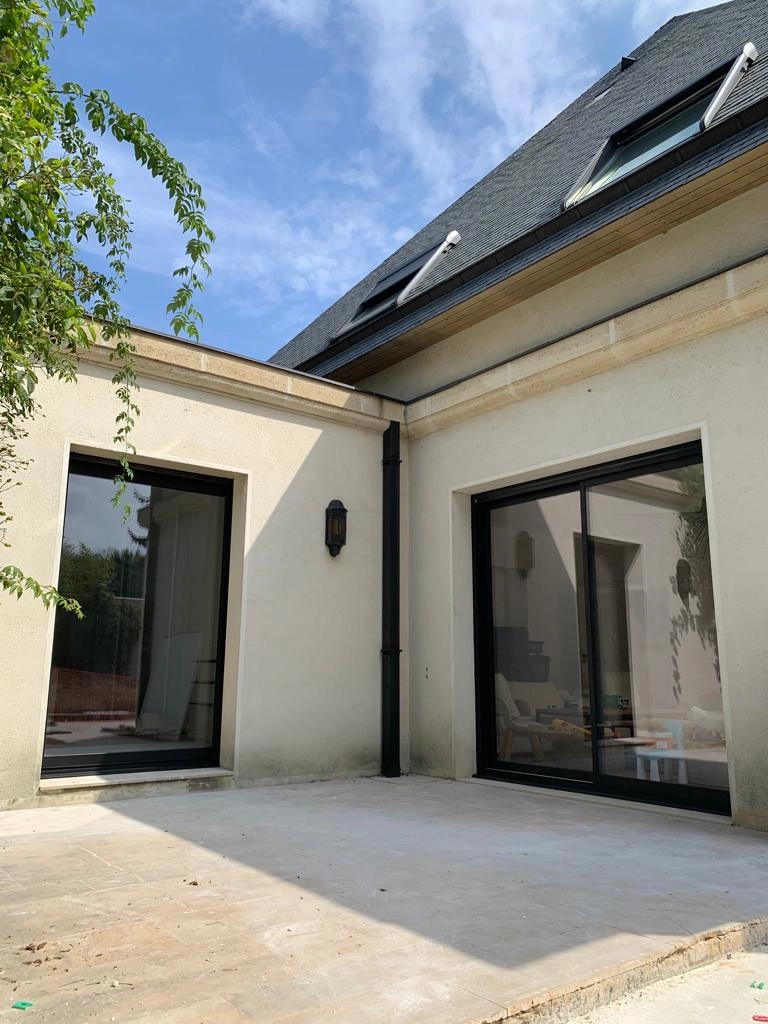 Baie coulissante alu noir et fenêtre fixe, façade beige pierre, toiture ardoise