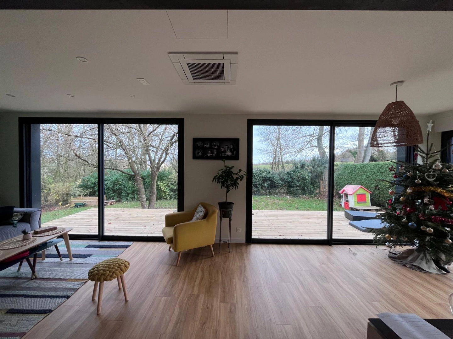 Double baie coulissante alu noire ouvrant sur terrasse bois et jardin depuis le salon