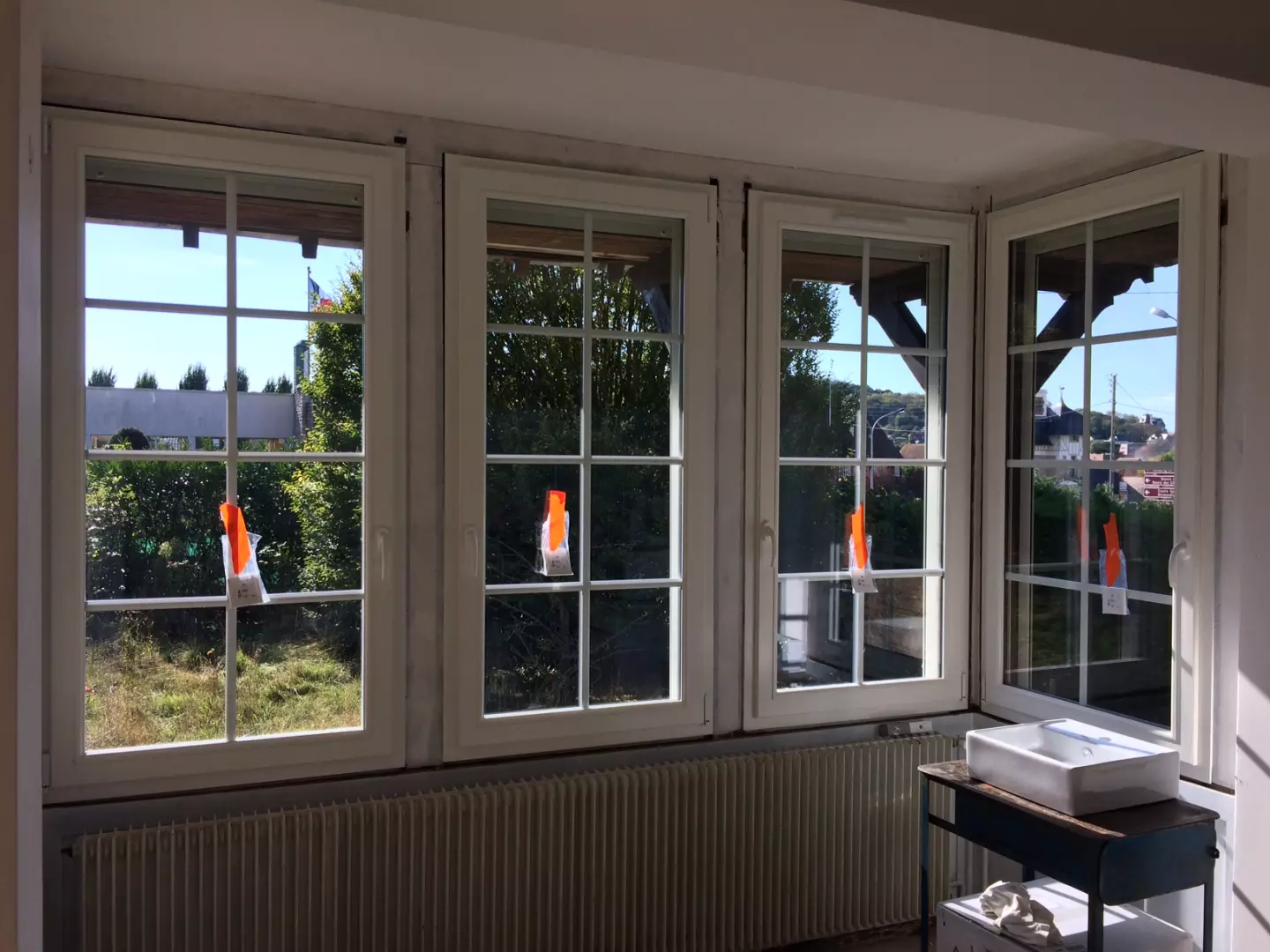 Quatre fenêtres blanches à petits bois en angle, radiateur sous appui, vue jardin ensoleillé