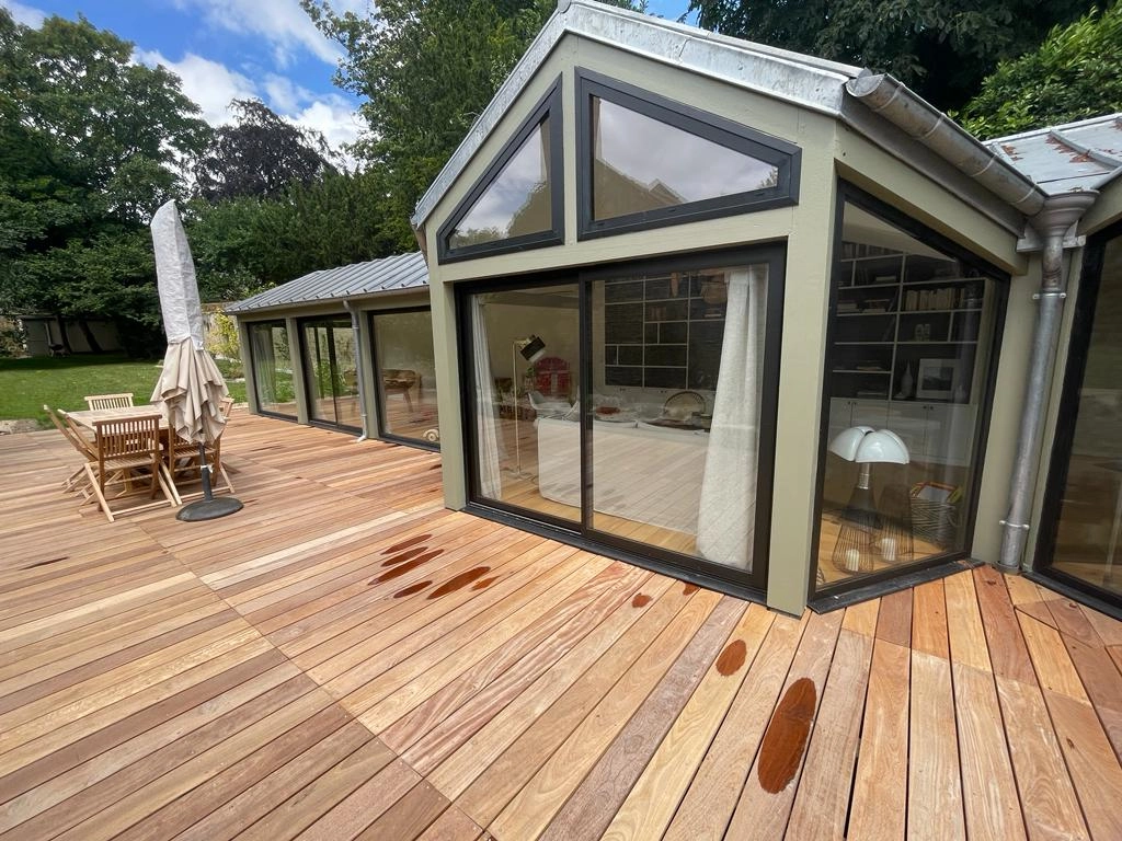 Extension façade vert olive, baies noires triangulaires, terrasse bois exotique