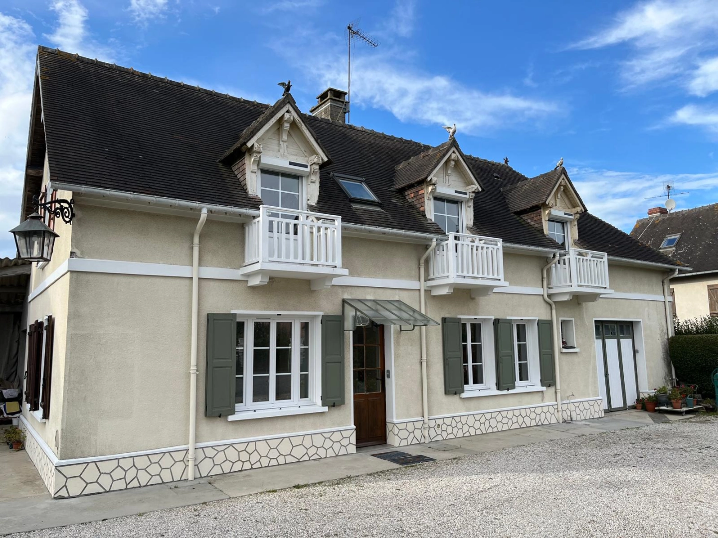 Maison crépi crème : fenêtres blanches, volets verts, garde-corps blancs aux lucarnes
