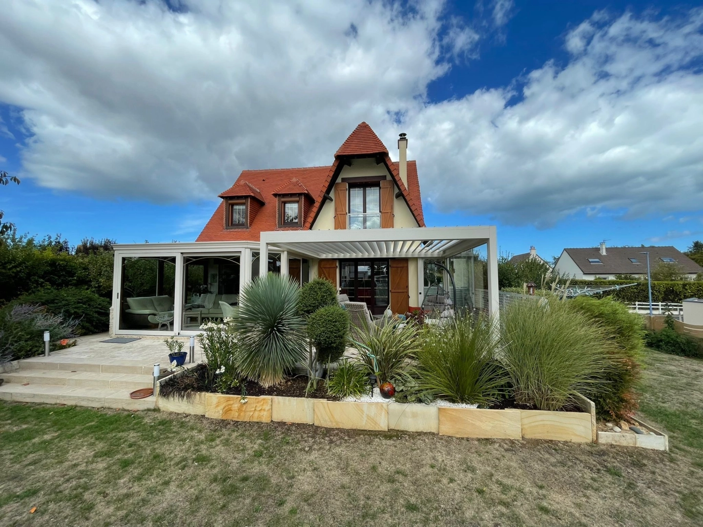 Véranda vitrée blanche et pergola bioclimatique adossés à maison tuiles rouges