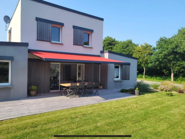 Store banne rouge déployé, volets coulissants gris, terrasse bois, maison bicolore