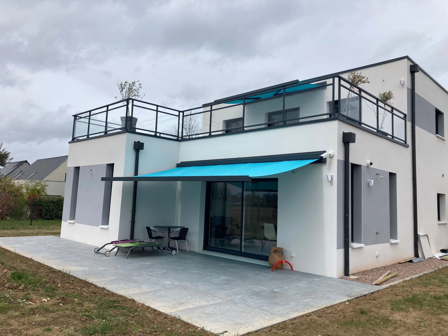 Maison moderne blanche : store banne turquoise déployé et garde-corps verre noir sur balcon