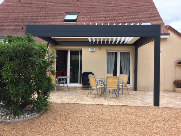 Pergola bioclimatique anthracite, lames blanches, terrasse pierre naturelle et salon