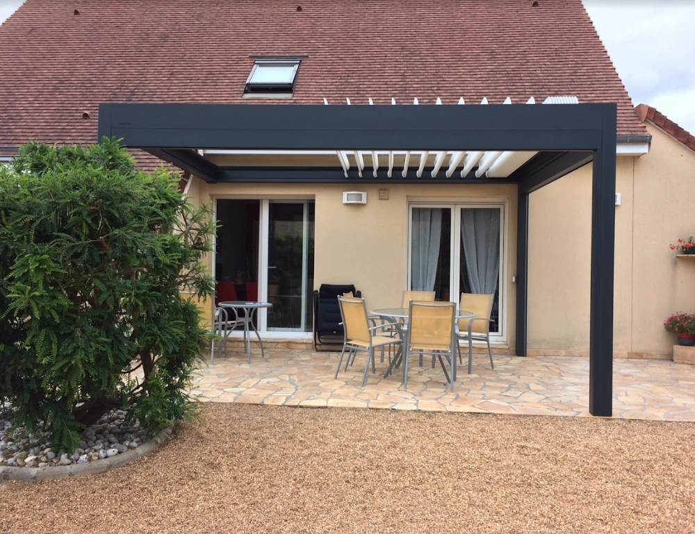 Pergola bioclimatique anthracite, lames blanches, terrasse pierre naturelle et salon
