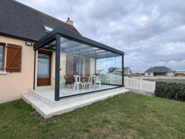 Pergola vitrée anthracite toit verre, terrasse carrelée claire et table en bois