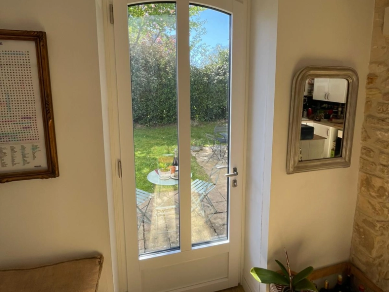 Porte-fenêtre blanche deux vitrages cintrée, vue jardin depuis intérieur rénové