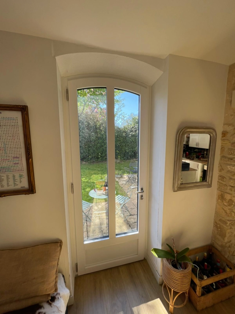 Porte-fenêtre blanche deux vitrages cintrée, vue jardin depuis intérieur rénové