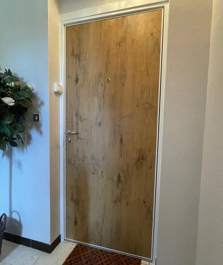 Porte d'entrée intérieure bois clair, cadre blanc, poignée inox, carrelage clair et tapis rouge