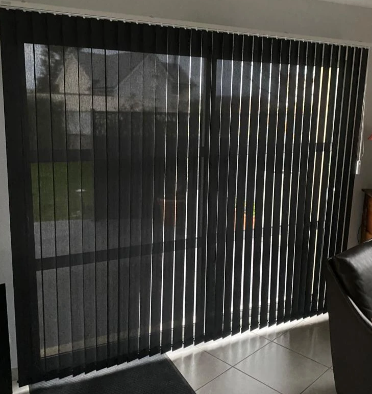 Stores verticaux noirs sur baie vitrée, lames fermées à gauche, ouvertes à droite, carrelage
