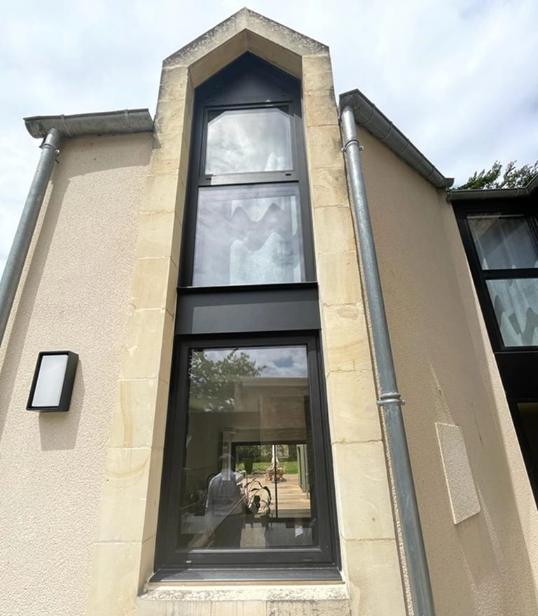 Fenêtre verticale cadres noirs dans encadrement pierre claire, façade enduit beige