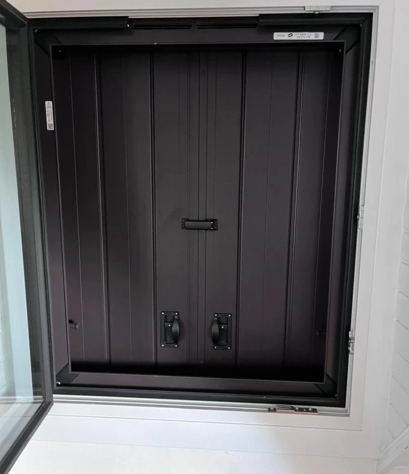Volet intérieur noir rainuré dans cadre blanc, fenêtre ouverte, poignées noires