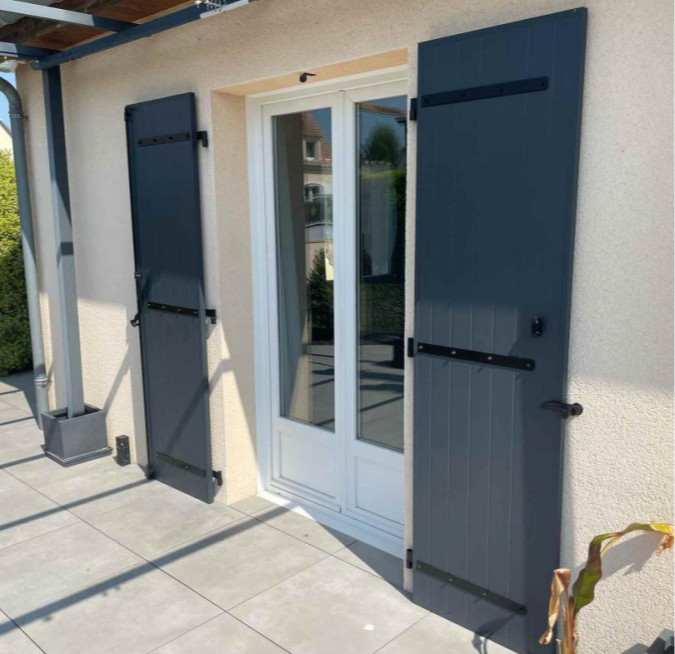 Volets battants anthracite ouverts, porte-fenêtre blanche, terrasse dalles, pergola alu